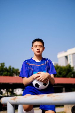 Bir çocuğun portre resmi tırabzana oturup elinde futbol topu tutuyordu..