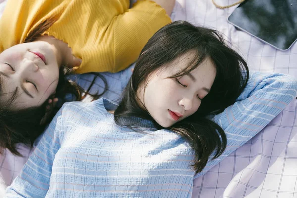 Two girls sleep on the mat during outdoor picnic.