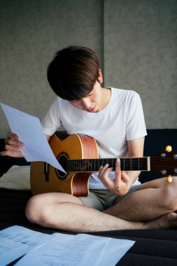 Genç Taylandlı gitarist akustik gitar çalışıyor ve yatak odasında şarkı sözü kağıdı notaları okuyor..