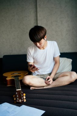 Genç Taylandlı gitarist Earphoens ile gitar çalmak için ilham kaynağı bulmak için akıllı telefon kullanan şarkılar dinliyor..