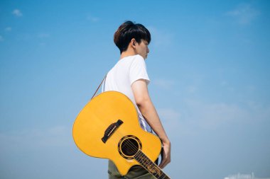 Sideview - Genç Taylandlı gitarist çatıda akustik gitar taşıyor.