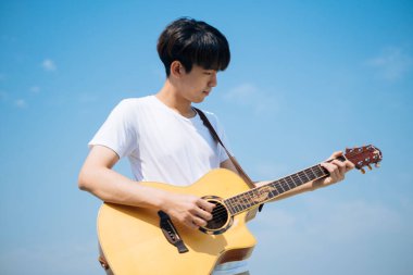 Genç Taylandlı gitarist çatıda akustik gitar çalıyor..