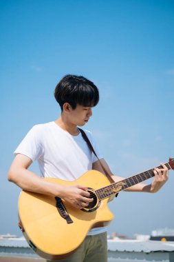 Genç Taylandlı gitarist çatıda akustik gitar çalıyor..