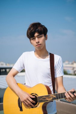Çatıda akustik gitaristli genç Taylandlı adamın portresi..