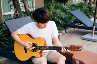 Genç Taylandlı gitarist plaj sandalyesinde akustik gitar çalıyor. Gezgin gitarcı..