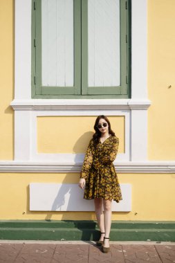 Sarı elbiseli tatlı kıvırcık saçlı kız Pastel binada dikey güneş gözlükleriyle dikiliyor..