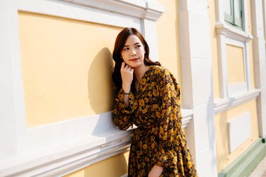 Sarı elbiseli tatlı kıvırcık saçlı kız. Parlak gülüşlü sarı ve beyaz binanın önünde duruyor..