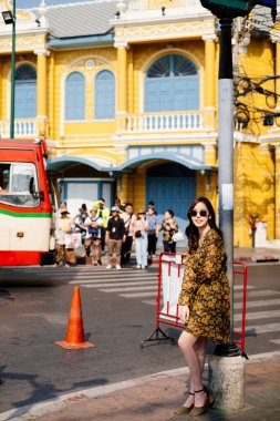 Sarı elbiseli ve güneş gözlüklü tatlı kıvırcık saçlı kız kırmızı barikatın yanındaki direğe yaslanmış..