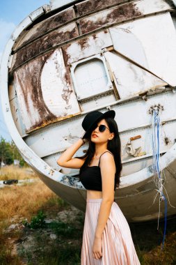 Makarna askılı ve enkaz uçağının önünde pembe etekli siyah uzun saçlı kızın portresi..