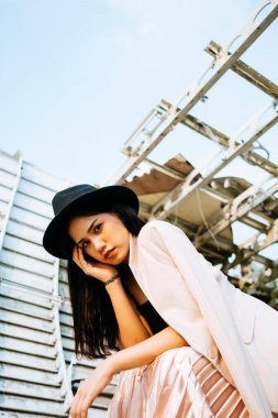 Siyah uzun saçlı kız mavi gökyüzünün altında siyah şapkalı enkaz uçakta oturuyor..