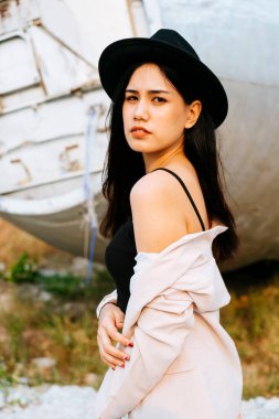 Siyah ve pembe elbiseli uzun saçlı kadın enkaz uçağının önünde dikilip ağzını kapatırken omzunu pembe elbisesiyle göster..