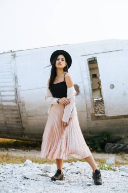 Siyah ve pembe elbiseli uzun saçlı kadın enkaz uçağının önünde dikilip ağzını kapatırken omzunu pembe elbisesiyle göster..
