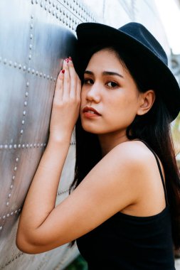 Siyah ve pembe elbiseli uzun saçlı kadın siyah şapkalı ve enkaz uçağının yanında oturuyor..