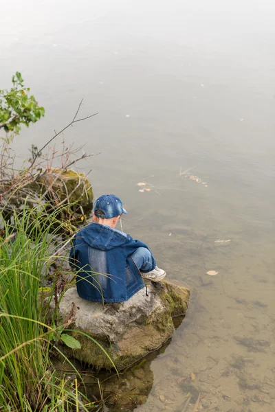 Ragazzo seduto sulle rive del fiume su una grande pietra — Foto Stock