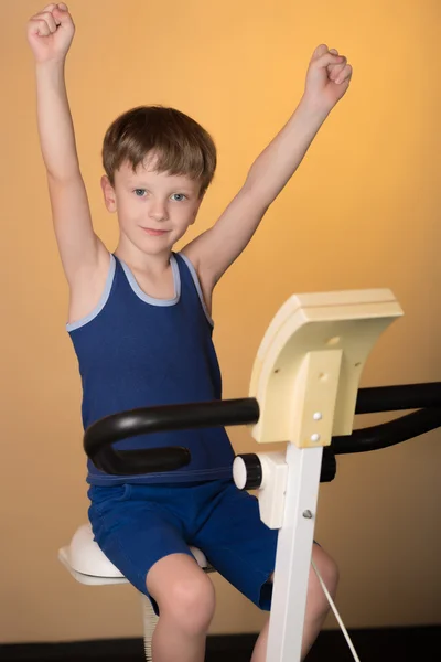 El niño está entrenado en una bicicleta estacionaria. Estilo de vida saludable . — Foto de Stock