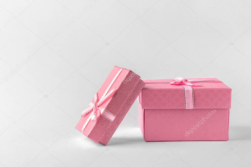 two pink gift boxes with ribbon and bow isolated on a white or light gray background, natural shadow, side view