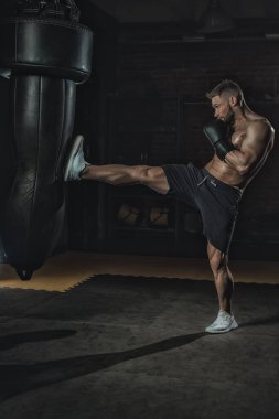 Siyah boks eldivenli dövüşçü, spor salonunda bacak yumruklayarak yener. Sıkı çalışan boksör, saldırganlık, terleme ve cilt parlatıcılığıyla, kopyalama alanı.