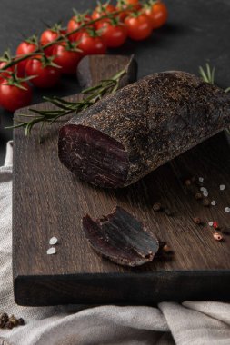 Bir tahta kesme tahtasının üzerinde kırmızı tütsülenmiş bir parça geyik eti, yan görüş, dikey fotoğraf...