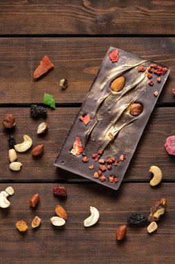 El yapımı siyah çikolata, badem, portakal ve kuru meyveler ahşap arka planda.