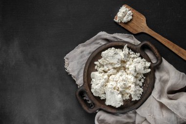Tahta bir tabakta spatula manzaralı taze süzme peynir. Gri çuval bezli koyu arkaplan, boşluğu kopyala