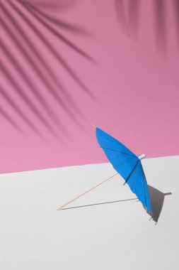 Beyaz ve pembe pastel renkleri olan yaz modeli. Mavi kumsal ya da öğle güneşinde kokteyl şemsiyesi ve fotokopi alanı için arka planda palmiye yapraklarının sert gölgeleri