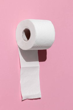 Pembe arka planda izole edilmiş beyaz bir tuvalet kağıdı rulosu. Öğlen güneşinin sert gölgeleri
