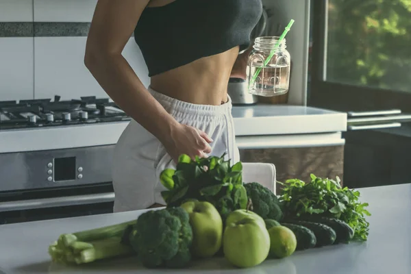 Fit woman drinking water, preparing vegetables for Green detox smoothie. Raw food diet.