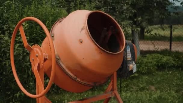 Kulübenin bölgesinde yeni turuncu beton karıştırıcı, evde çimento karıştırmak için küçük taşınabilir makine. Çimento karışımı. Yeşil bulanık arkaplan — Stok video