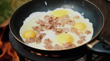 Kızartma tavasında yumurta ve pastırma, bulanık arka planda yeşil çimen, ızgarada pişmiş, yaz kahvaltısı, doğada yemek, doğa ve ekoloji kavramı. Yavaş çekim.