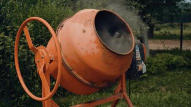 Kulübenin bölgesinde yeni turuncu beton karıştırıcı, evde çimento karıştırmak için küçük taşınabilir makine. Çimento karışımı. Yeşil bulanık arkaplan
