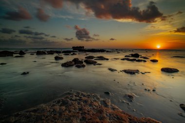 Arka plan için inanılmaz bir deniz manzarası. Taşları ve taşları olan bir sahil. Dalgalar çekildi. Hareket suyu. Açık renkli gökyüzü. Kapama hızı yavaş. Yumuşak odaklanma. Mengening Plajı, Bali, Endonezya