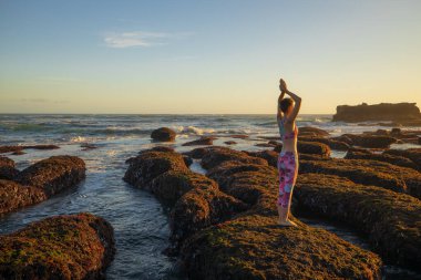 Beyaz kadın gelgit sırasında büyük bir taşın üzerinde duruyor. Yoga ve plajda meditasyon. Namaste Mudra.Bali 'de yoga inzivası. Açık hava aktiviteleri. Okyanus manzaralı. Mengening Plajı