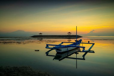 Deniz Burnu. Geleneksel balıkçı teknesi Jung. Gün doğumu manzarası. Okyanustaki bir adada çardaklar. Su yansıması. Kapama hızı yavaş. Yumuşak odaklanma. Sanur Plajı, Bali, Endonezya.