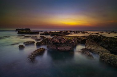 Arka plan için inanılmaz bir deniz manzarası. Taşları ve taşları olan bir sahil. Dalgalar çekildi. Hareket suyu. Gökyüzü açık. Güneş ufukta görünüyor. Peyzaj arka planı. Kapama hızı yavaş. Yumuşak odaklanma. Mengening Plajı, Bali, Endonezya