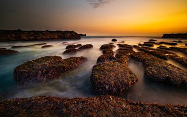 Arka plan için inanılmaz bir deniz manzarası. Taşları ve taşları olan bir sahil. Dalgalar çekildi. Hareket suyu. Gökyüzü açık. Güneş ufukta görünüyor. Peyzaj arka planı. Kapama hızı yavaş. Yumuşak odaklanma. Mengening Plajı, Bali, Endonezya