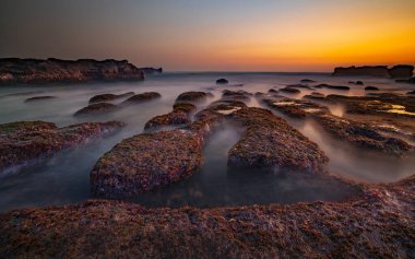 Arka plan için inanılmaz bir deniz manzarası. Taşları ve taşları olan bir sahil. Dalgalar çekildi. Hareket suyu. Gökyüzü açık. Güneş ufukta görünüyor. Peyzaj arka planı. Kapama hızı yavaş. Yumuşak odaklanma. Mengening Plajı, Bali, Endonezya
