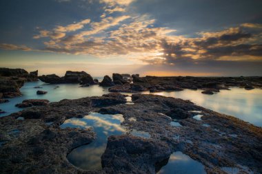 Güzel deniz manzarası. Dalgalar çekildiğinde kayalık kumsalda uzun süre kalmak. Panoramik okyanus manzarası. Doğanın bileşimi. Günbatımı manzara arka planı. Bulutlu gökyüzü. Su yansıması. Mengening Plajı, Bali, Endonezya