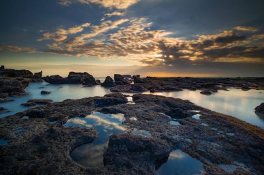 Güzel deniz manzarası. Dalgalar çekildiğinde kayalık kumsalda uzun süre kalmak. Panoramik okyanus manzarası. Doğanın bileşimi. Günbatımı manzara arka planı. Bulutlu gökyüzü. Su yansıması. Mengening Plajı, Bali, Endonezya