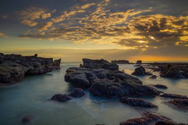 Güzel deniz manzarası. Dalgalar çekildiğinde kayalık kumsalda uzun süre kalmak. Panoramik okyanus manzarası. Doğanın bileşimi. Günbatımı manzara arka planı. Bulutlu gökyüzü. Su yansıması. Mengening Plajı, Bali, Endonezya