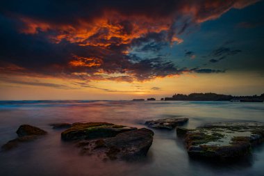 Sakin okyanus uzun süre maruz kaldı. Deniz dalgalarının gizemli sisinde taşlar. Doğa geçmişi kavramı. Günbatımı manzara arka planı. Bulutlu gökyüzü. Yumuşak odaklanma. Mengening Plajı, Bali, Endonezya.