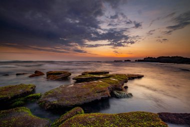 Sakin okyanus uzun süre maruz kaldı. Deniz dalgalarının gizemli sisinde taşlar. Doğa geçmişi kavramı. Günbatımı manzara arka planı. Bulutlu gökyüzü. Yumuşak odaklanma. Mengening Plajı, Bali, Endonezya.