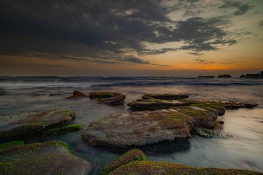Sakin okyanus uzun süre maruz kaldı. Deniz dalgalarının gizemli sisinde taşlar. Doğa geçmişi kavramı. Günbatımı manzara arka planı. Bulutlu gökyüzü. Yumuşak odaklanma. Mengening Plajı, Bali, Endonezya.