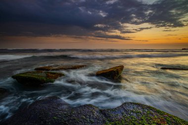 Hareket dalgalarıyla inanılmaz bir deniz manzarası. Waterscape arka planı. Hareket eden su. Doğa konsepti. Günbatımı manzara arka planı. Taşları ve taşları olan bir sahil. Uzun pozlama. Yumuşak odaklanma. Mengening Plajı, Bali.
