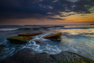 Hareket dalgalarıyla inanılmaz bir deniz manzarası. Waterscape arka planı. Hareket eden su. Doğa konsepti. Günbatımı manzara arka planı. Taşları ve taşları olan bir sahil. Uzun pozlama. Yumuşak odaklanma. Mengening Plajı, Bali.