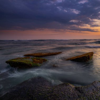 Hareket dalgalarıyla inanılmaz bir deniz manzarası. Waterscape arka planı. Hareket eden su. Doğa konsepti. Günbatımı manzara arka planı. Taşları ve taşları olan bir sahil. Uzun pozlama. Yumuşak odaklanma. Mengening Plajı, Bali.