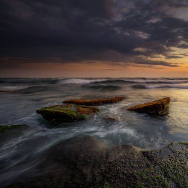 Hareket dalgalarıyla inanılmaz bir deniz manzarası. Waterscape arka planı. Hareket eden su. Doğa konsepti. Günbatımı manzara arka planı. Taşları ve taşları olan bir sahil. Uzun pozlama. Yumuşak odaklanma. Mengening Plajı, Bali.