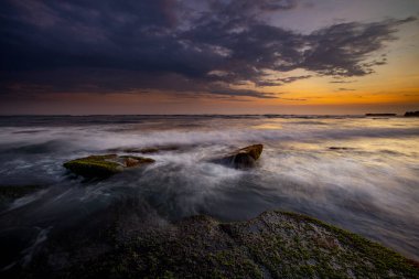 Hareket dalgalarıyla inanılmaz bir deniz manzarası. Waterscape arka planı. Hareket eden su. Doğa konsepti. Günbatımı manzara arka planı. Taşları ve taşları olan bir sahil. Uzun pozlama. Yumuşak odaklanma. Mengening Plajı, Bali.