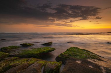 Sakin okyanus uzun süre maruz kaldı. Deniz dalgalarının gizemli sisleriyle kaplanmış taşlarla. Doğa geçmişi kavramı. Günbatımı manzara arka planı. Yumuşak odaklanma. Mengening Plajı, Bali, Endonezya.
