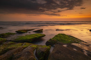 Sakin okyanus uzun süre maruz kaldı. Deniz dalgalarının gizemli sisleriyle kaplanmış taşlarla. Doğa geçmişi kavramı. Günbatımı manzara arka planı. Yumuşak odaklanma. Mengening Plajı, Bali, Endonezya.