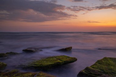 Sakin okyanus uzun süre maruz kaldı. Deniz dalgalarının gizemli sisleriyle kaplanmış taşlarla. Doğa geçmişi kavramı. Günbatımı manzara arka planı. Yumuşak odaklanma. Mengening Plajı, Bali, Endonezya.